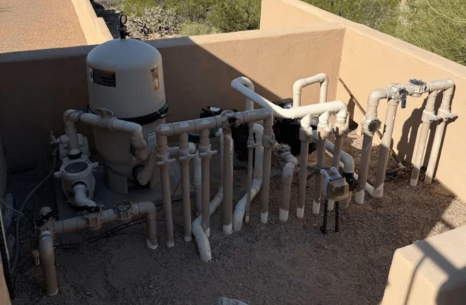 Pool equipment pad with plumbing, valves and filter housing against a block wall