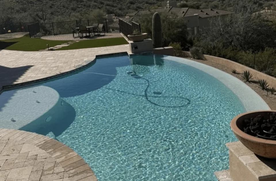 Free-form desert pool with travertine decking and saguaro cactus, typical of the Mesa-area pools we service