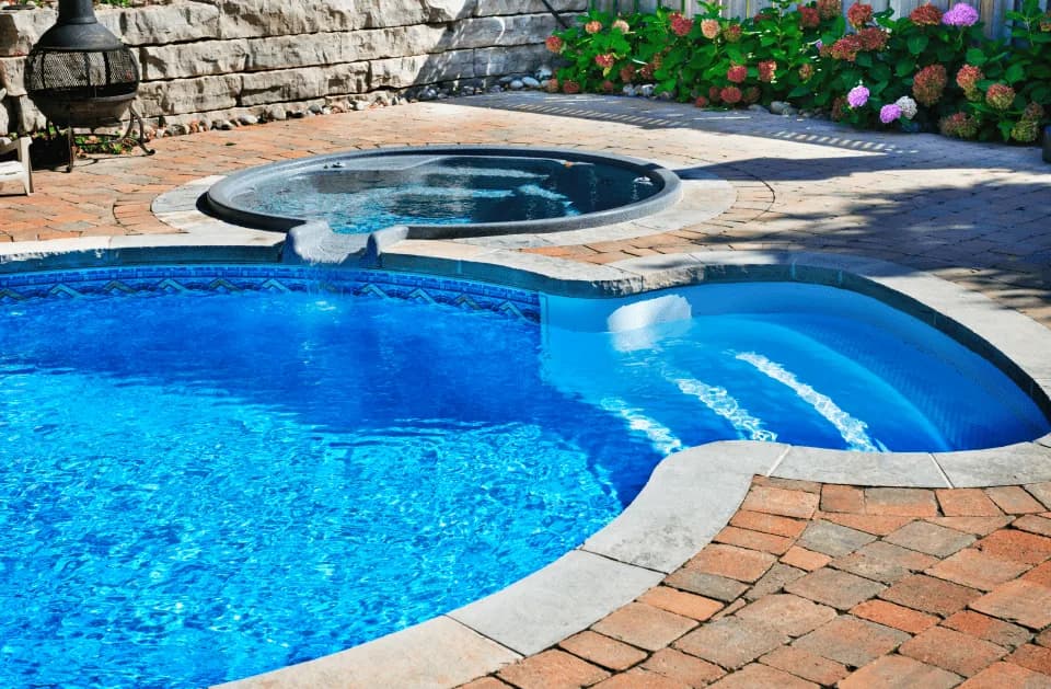 Curved pool and raised spa with a spillway, surrounded by brick paver decking