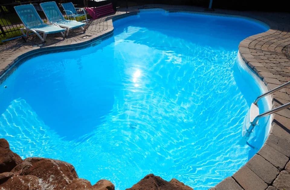Clear blue swimming pool with stone coping and patio seating